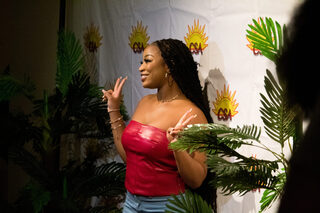 An audience member poses in front of the Caribbean Student Association backdrop at the front doors of Goldstein Auditorium. Many people stopped by to commemorate the moment by taking photos to show off their friends, outfits and prizes won during event giveaways.